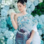 Woman in traditional Thai attire amidst a lush floral backdrop, embodying beauty and culture.